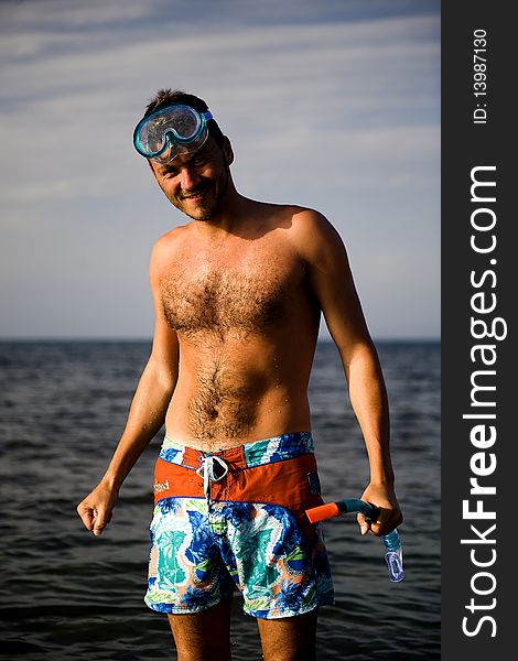 Young happy handsome summer diving man with swimming mask and snorkel preparing to dive in blue sea