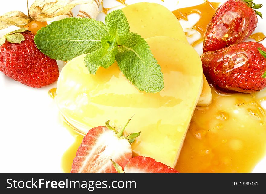 Creme caramel in heart-shape on a mirror of caramel splashes, decorated with strawberries, physalis and mint leaves. Creme caramel in heart-shape on a mirror of caramel splashes, decorated with strawberries, physalis and mint leaves