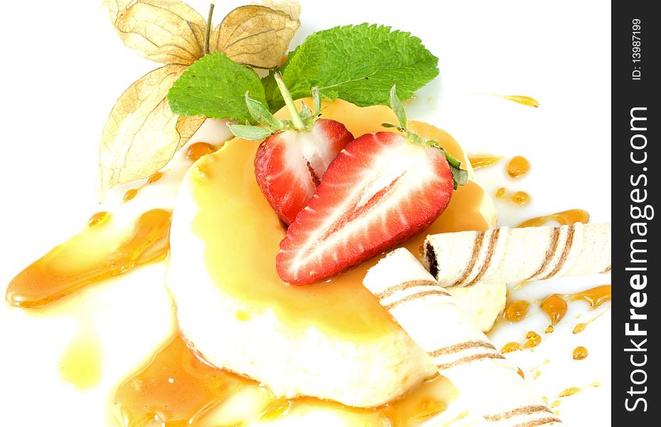Creme caramel on a mirror of caramel splashes, decorated with strawberries, physalis, biscuit rolls and mint leaves