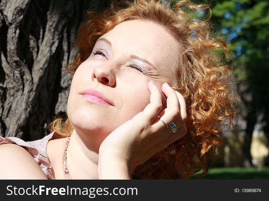 Portrait of the red hair girl near the tree in a park