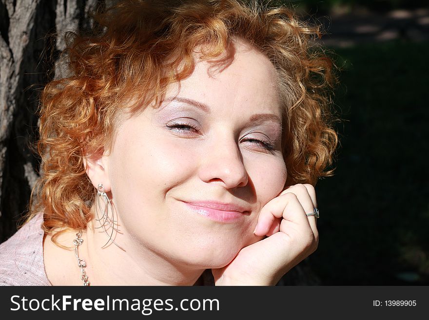 Portrait of the red hair girl near the tree in a park