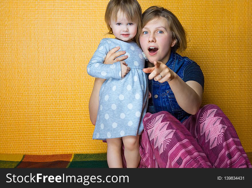 Portrait of mother hugging toddler daughter. pretty, amazed girl look to camera. woman, person point at surprise by
