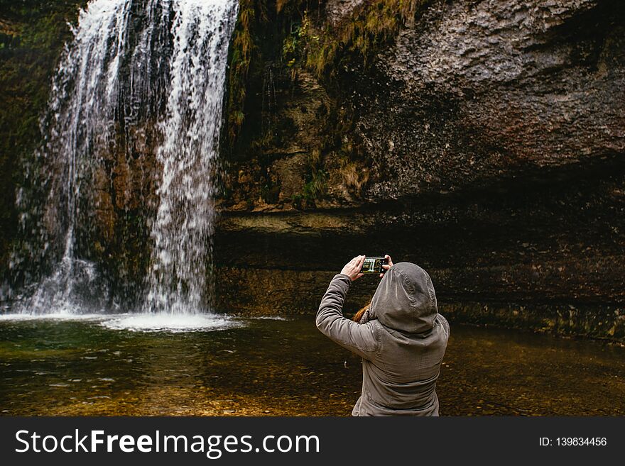 Woman taking a picture of a waterfall in a forest. Cascades du Hérisson, France.