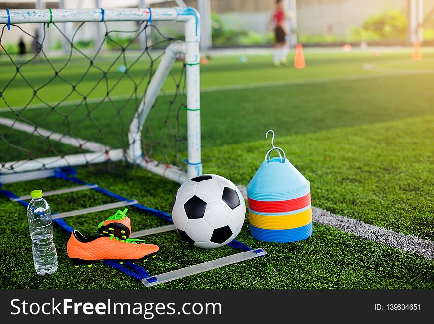 Goal, soccer ball, marker cones, sports shoes and bottle water on green artificial turf for soccer training equipment