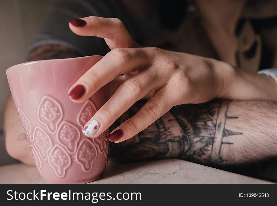 Close up female hand with red nails holding pink cup of tea or coffe