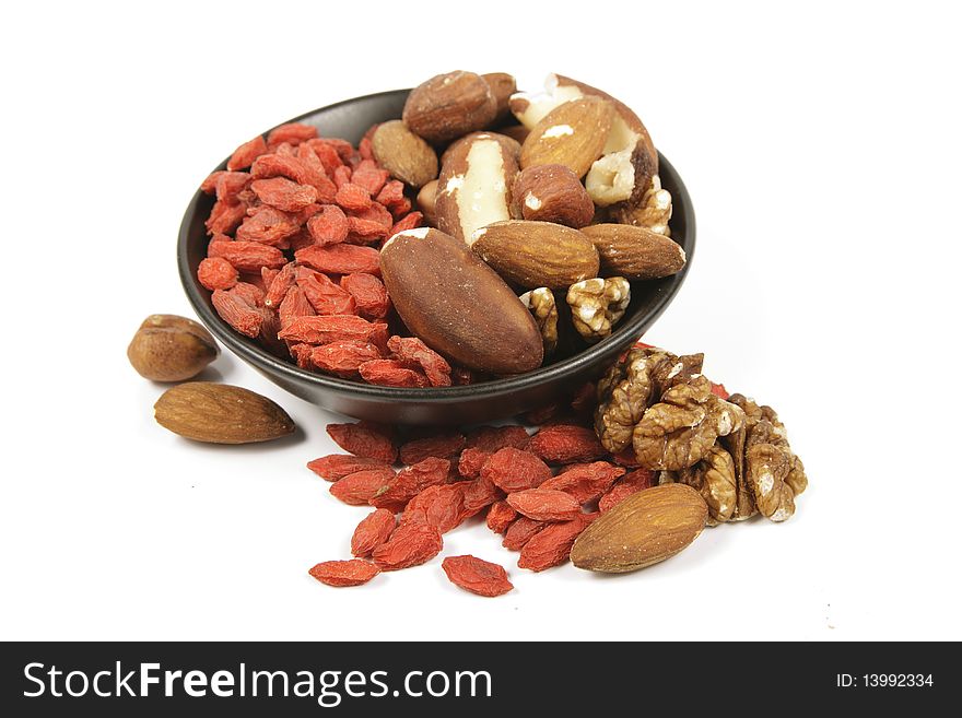 Red dry goji berries with mixed nuts in a small black bowl on a reflective white background. Red dry goji berries with mixed nuts in a small black bowl on a reflective white background