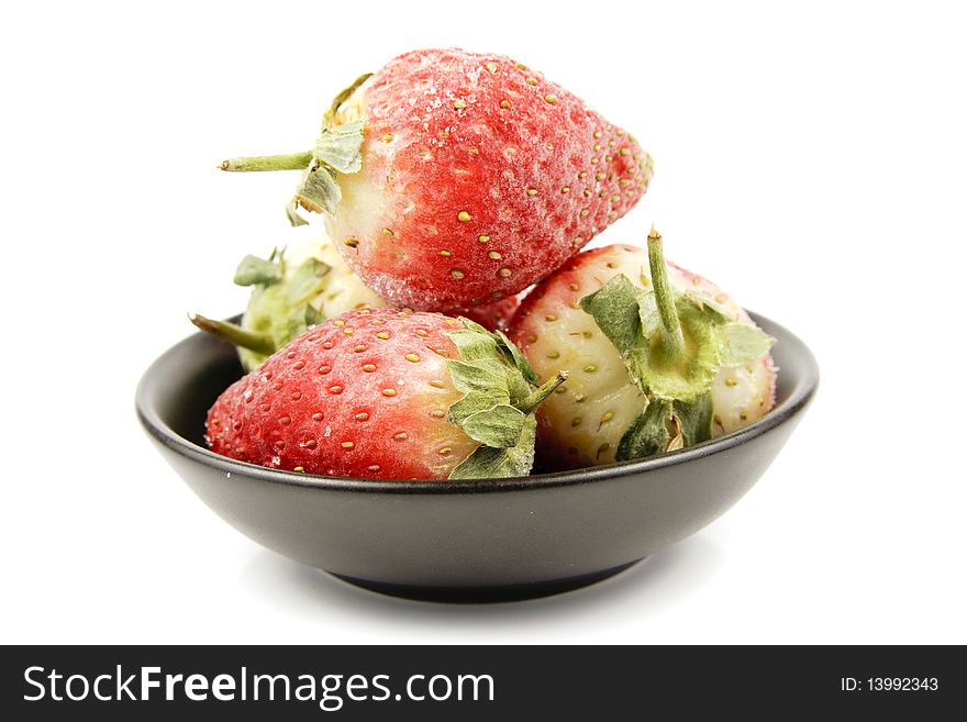 Red ripe frozen strawberries in a small black bowl on a reflective white background. Red ripe frozen strawberries in a small black bowl on a reflective white background