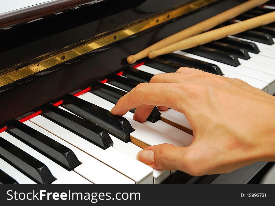 Right hand playing on black and white piano keyboard with drum sticks. For concepts like music and creativity. Right hand playing on black and white piano keyboard with drum sticks. For concepts like music and creativity.