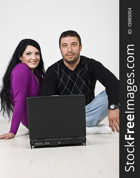 Couple sitting on wooden floor and using a laptop,both looking at camera,see more in. Couple sitting on wooden floor and using a laptop,both looking at camera,see more in