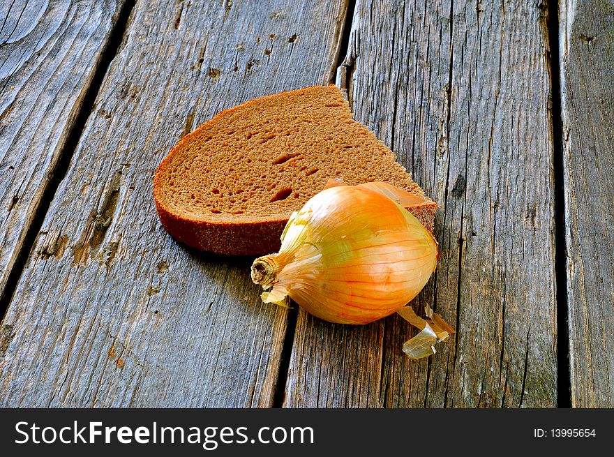 A piece of black bread and a slice of onion on an old wooden table. A piece of black bread and a slice of onion on an old wooden table