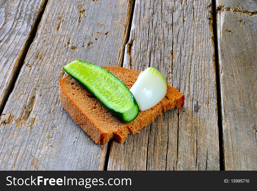A slice of black bread, onion and cucumber on an old wooden table. A slice of black bread, onion and cucumber on an old wooden table
