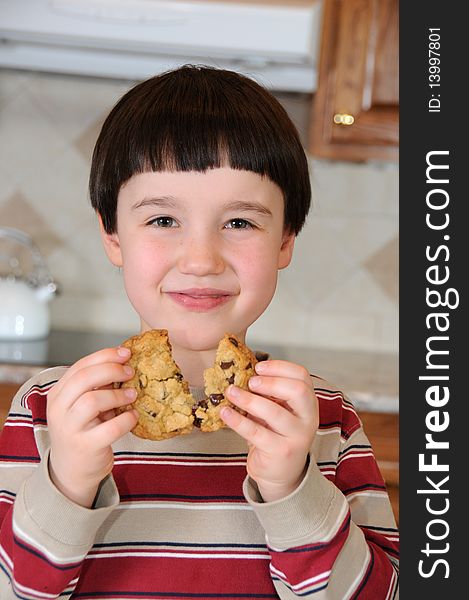 A little boy smiles as he breaks a chocolate chip cookie before eating it. A little boy smiles as he breaks a chocolate chip cookie before eating it