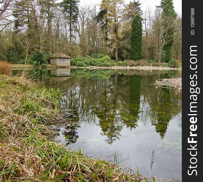 A cottage on the side of the lake at Wallington. With grass in the foreground and reflections in the lake of the building and trees. A cottage on the side of the lake at Wallington. With grass in the foreground and reflections in the lake of the building and trees.