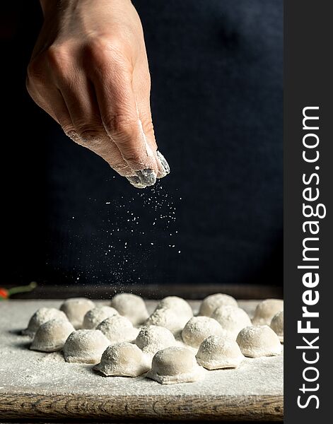 Uzbek national food Chuchvara, like dumplings, lie in the shape of a heart, on a wooden board, hands are crushing flour from above. Vertical frame