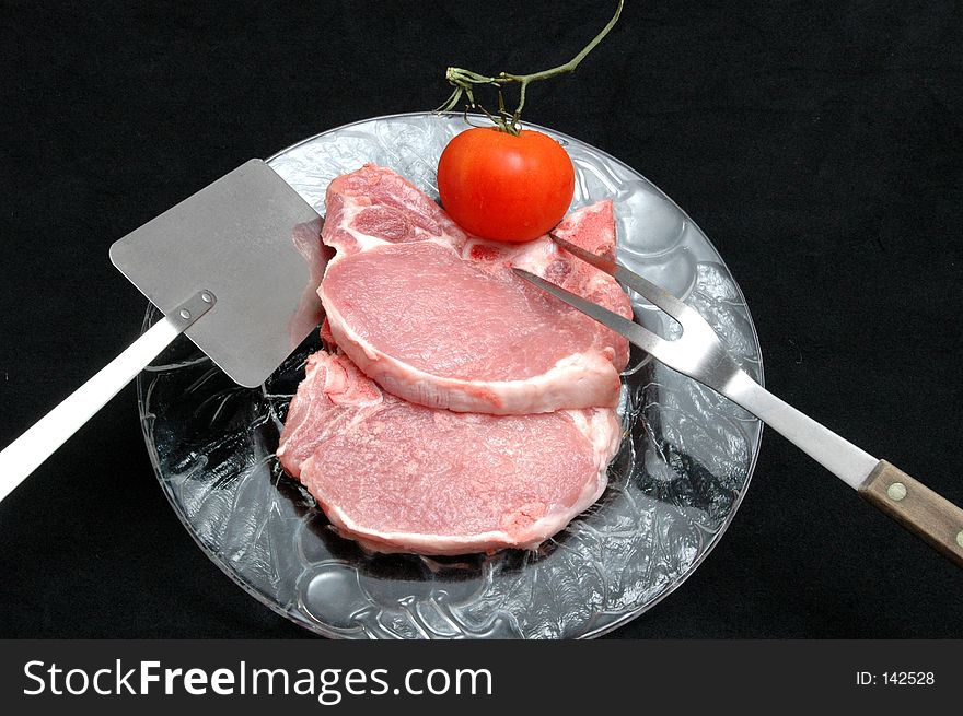 Two center cut pork chops, tomato and tools on a clear plate