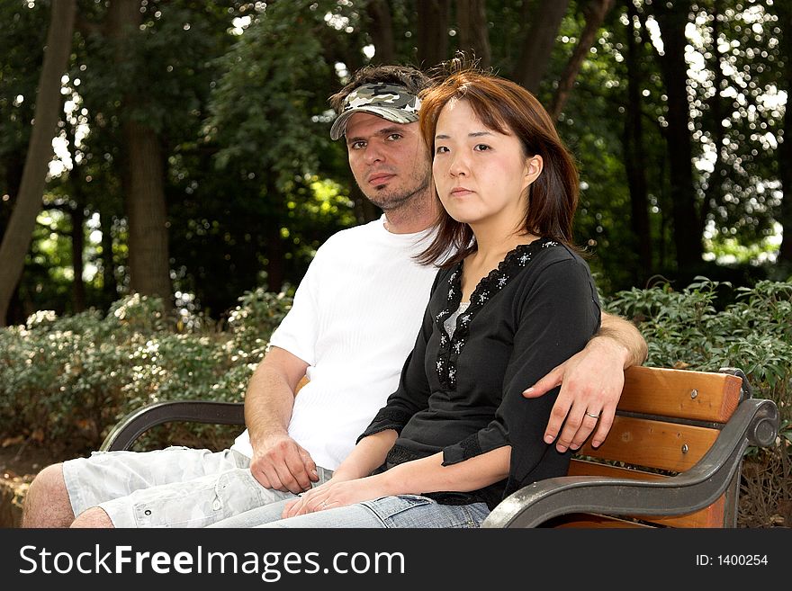 Interracial couple sitting together on a park bench. Interracial couple sitting together on a park bench