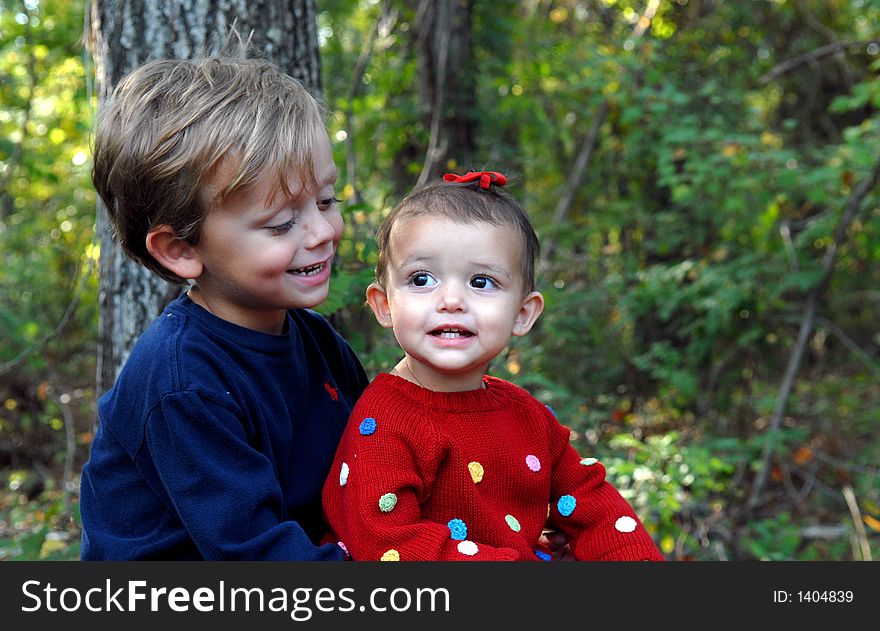 A little girl smiling and a young boy looking at her  in an outdoor setting. A little girl smiling and a young boy looking at her  in an outdoor setting.