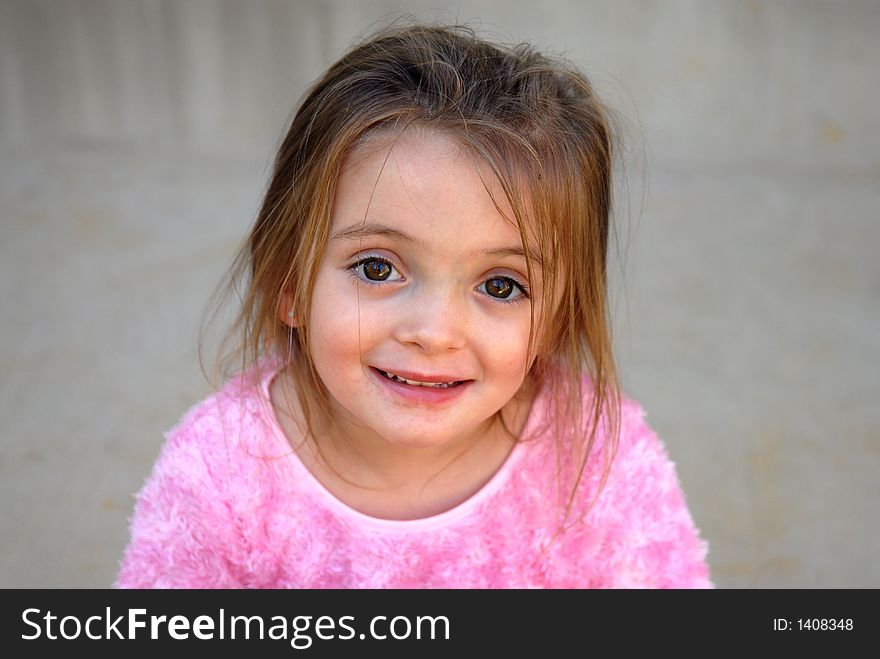 A pretty little girl dressed in a fuzzy pink shirt with a sweet smile and big brown eyes.