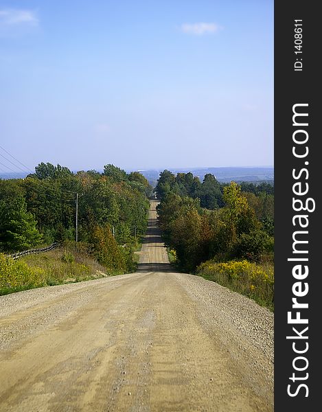 Looking down a sloped treelined country dirt road against a blue sky background. Looking down a sloped treelined country dirt road against a blue sky background