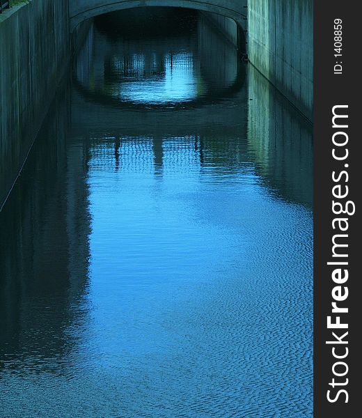 Inner city canal & the reflection of the canal walls & bridge on the water.