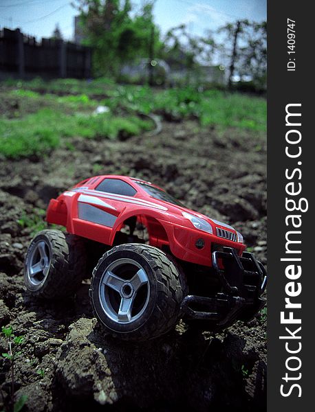 Toy off-road car on ground overcoming obstacle, with slight vignette and perspective. Film scan.