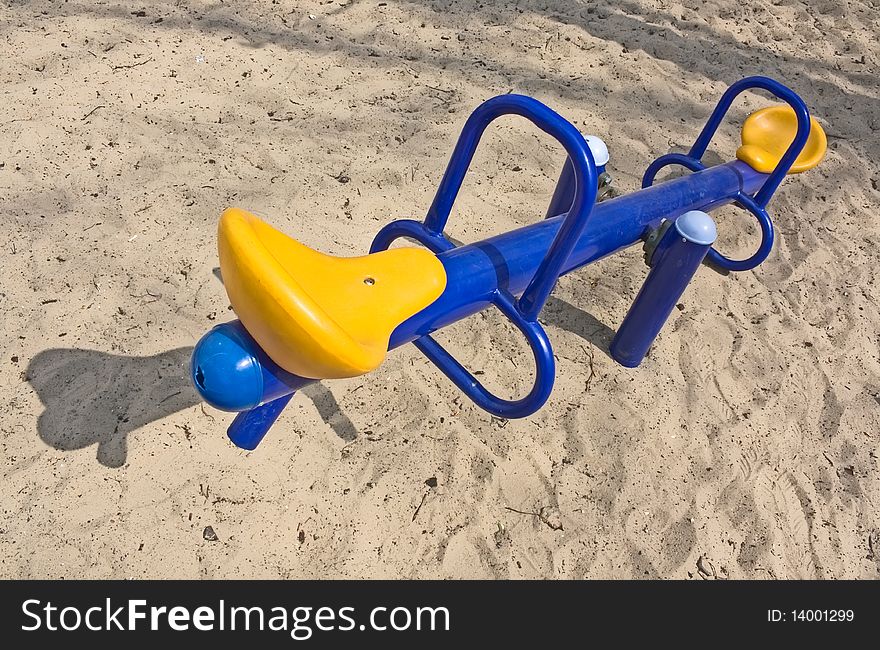 An empty blue seesaw with yellow seats in a playground. An empty blue seesaw with yellow seats in a playground