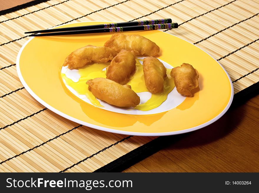 Yellow plate with chicken, lemon sauce and chopsticks on bamboo placemat.  Horizontal. Yellow plate with chicken, lemon sauce and chopsticks on bamboo placemat.  Horizontal.