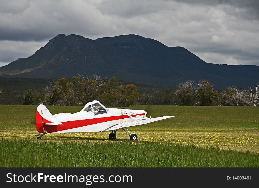 White and red glider tow plane spotlighted by sun in bright green wheat field, with a contrasting moody back drop of a mountain and foreboding sky. White and red glider tow plane spotlighted by sun in bright green wheat field, with a contrasting moody back drop of a mountain and foreboding sky.