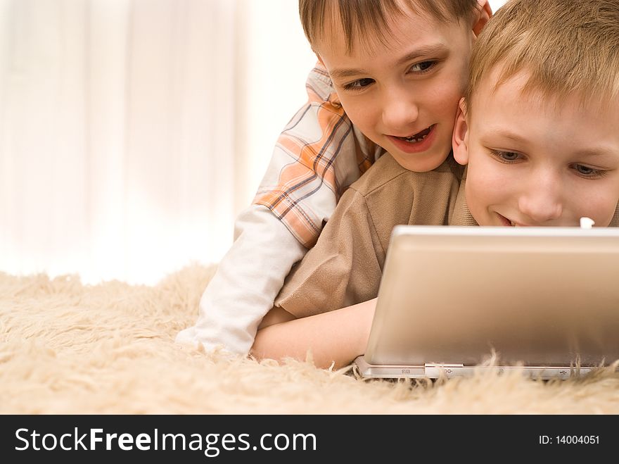 Two  brothers lie on the carpet with laptop. Two  brothers lie on the carpet with laptop