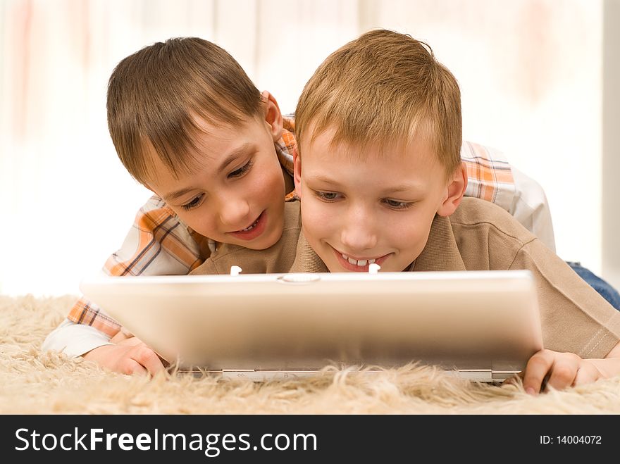 Two brothers lie on the carpet with laptop. Two brothers lie on the carpet with laptop