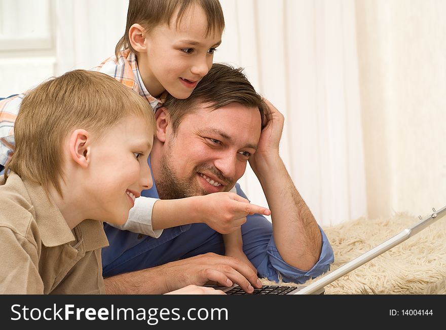 Father with his sons is on the carpet with laptop