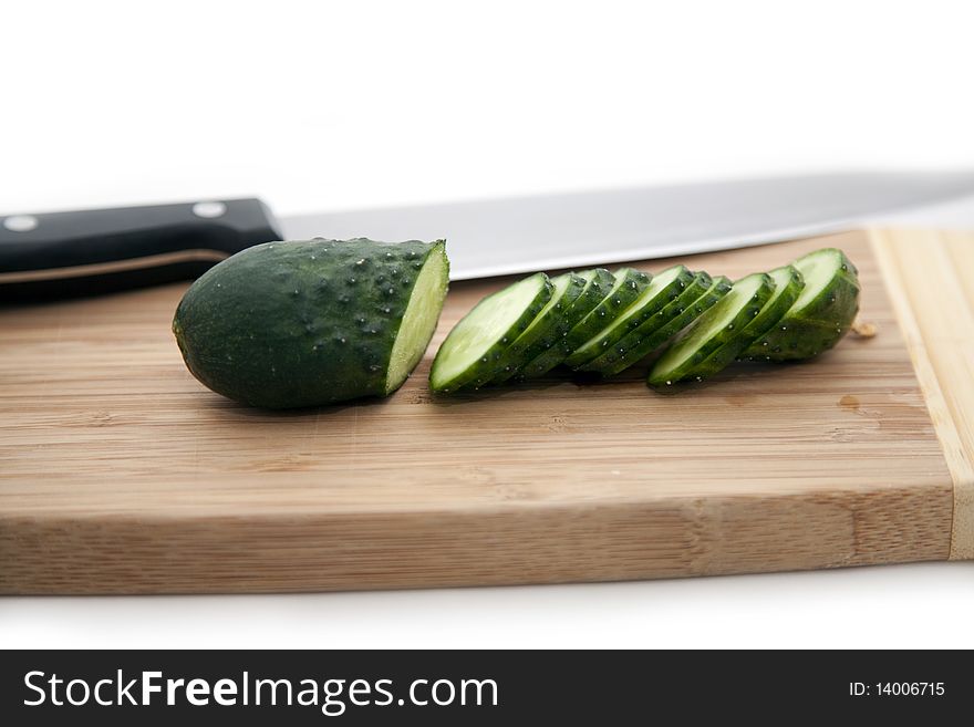 The green cucumber cut on segments and a knife on a bamboo board. The green cucumber cut on segments and a knife on a bamboo board