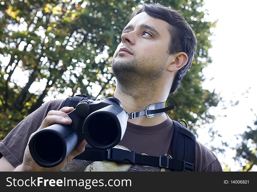 Young male bird watcher holding binoculars looking around. Young male bird watcher holding binoculars looking around