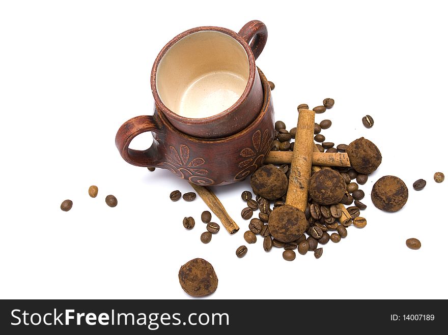 Two ceramic handmade cups with coffee beans, sticks of cinnamon and sweet chocolates isolated on white background. Two ceramic handmade cups with coffee beans, sticks of cinnamon and sweet chocolates isolated on white background