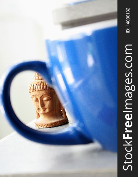 A Buddha head looks through a blue coffee mug. A Buddha head looks through a blue coffee mug