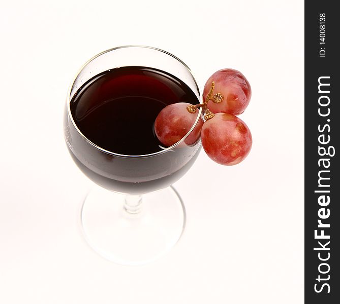 Red wine in a wineglass with three red grapes on white background