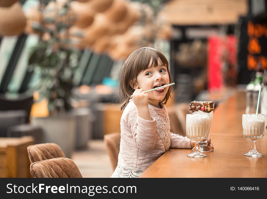 Charming Funny little girl drinks a milkshake in a restaurant, licking a tube. Baby food fast food . Leisure in the cafe