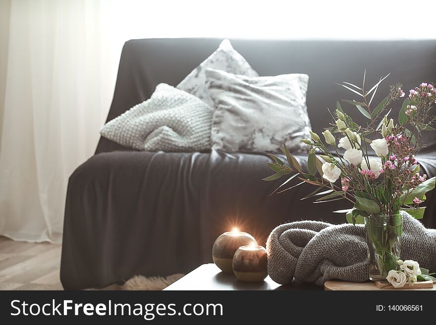 Cozy home interior with elements of decor in the living room with a black sofa and a vase of flowers and lighted candles on a small table. Cozy home interior with elements of decor in the living room with a black sofa and a vase of flowers and lighted candles on a small table