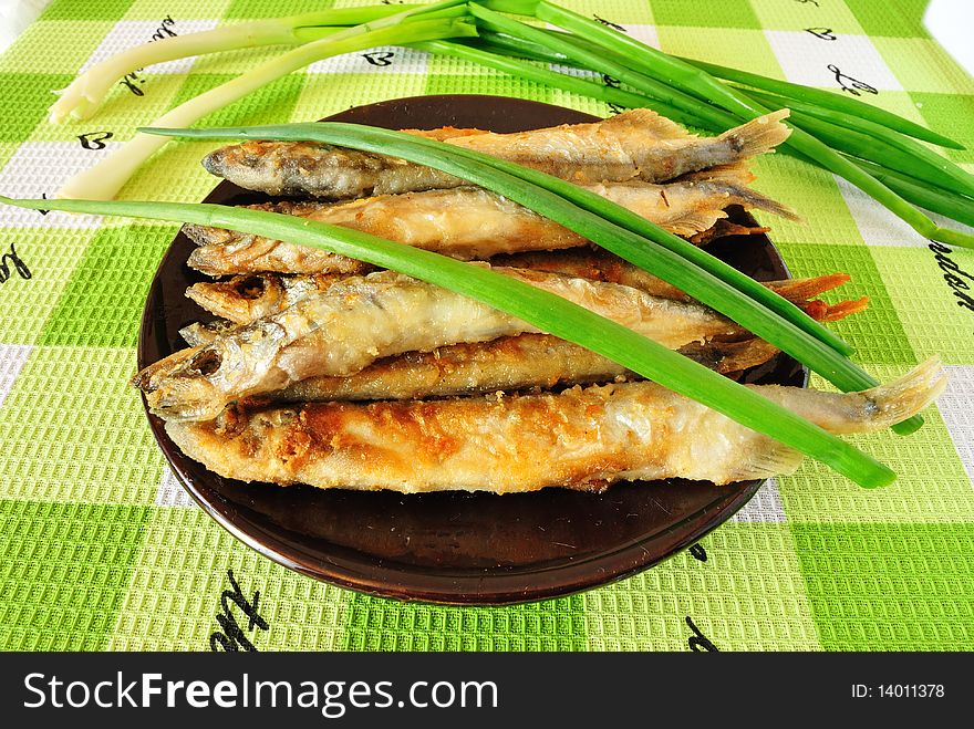 Image of fried fish capelin in the saucer with green onions. Image of fried fish capelin in the saucer with green onions