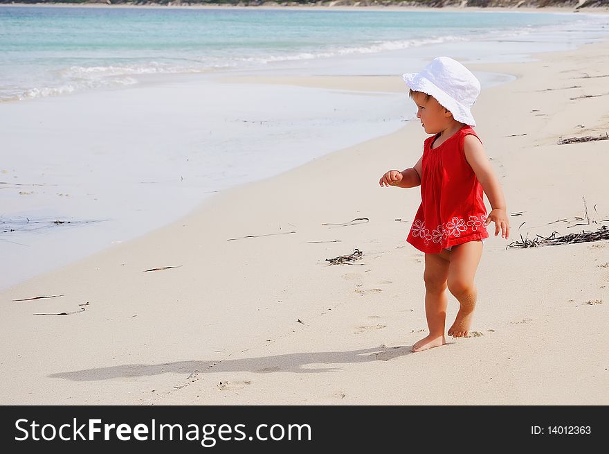 Little happy girl in a red dress and a white Panama hat on the beach