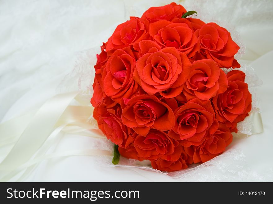 The round bouquet of red roses on white silk is decorated by satiny tapes