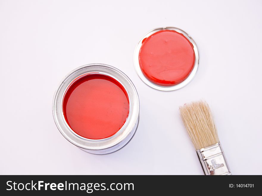 A can of red paint with a brush on top with a red coloured tip. A can of red paint with a brush on top with a red coloured tip