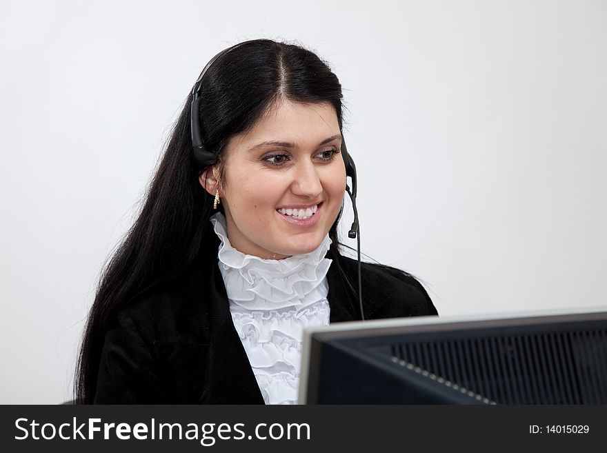 Young smiling brunette woman with headphones sits at a table in front of the monitor. Young smiling brunette woman with headphones sits at a table in front of the monitor.