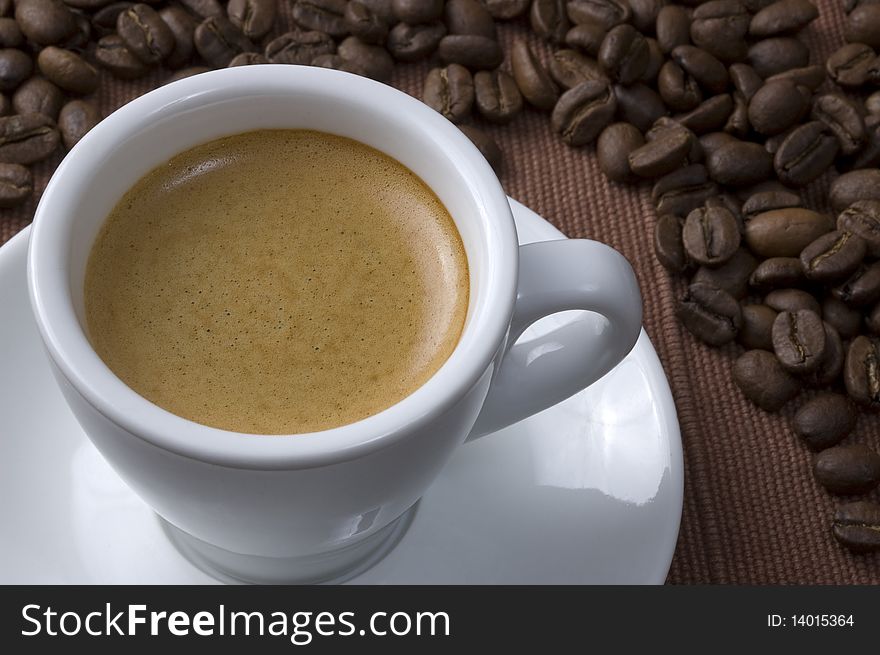 Coffee cup and coffee beans over brown textured fabric. Coffee cup and coffee beans over brown textured fabric