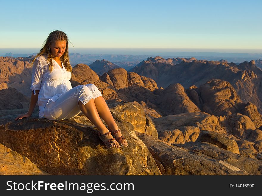 A girl sitting on a mountaintop in the setting sun. A girl sitting on a mountaintop in the setting sun