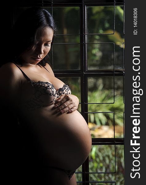 Woman holds her pregnant belly and stands at the window. Woman holds her pregnant belly and stands at the window