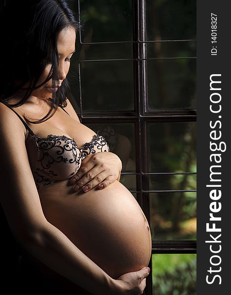 Woman holds her pregnant belly and stands at the window. Woman holds her pregnant belly and stands at the window