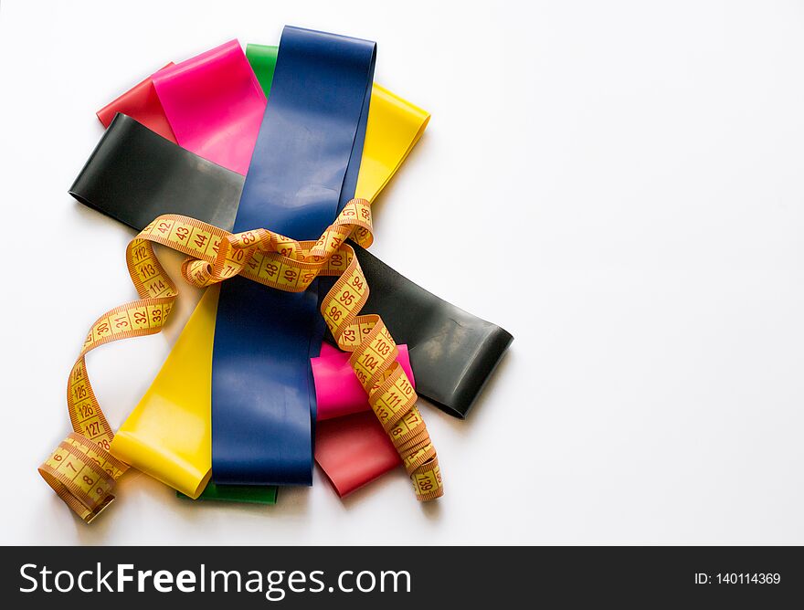 Colorful fitness gums tied up with meter tape isolated on white background. Sport concept - elastic expanders of different colors