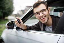 Satisfied Young Guy Is Peeking From The Car Window While Looking At The Camera. He Is Holding The Keys At His Right Hand. Lottery Stock Images