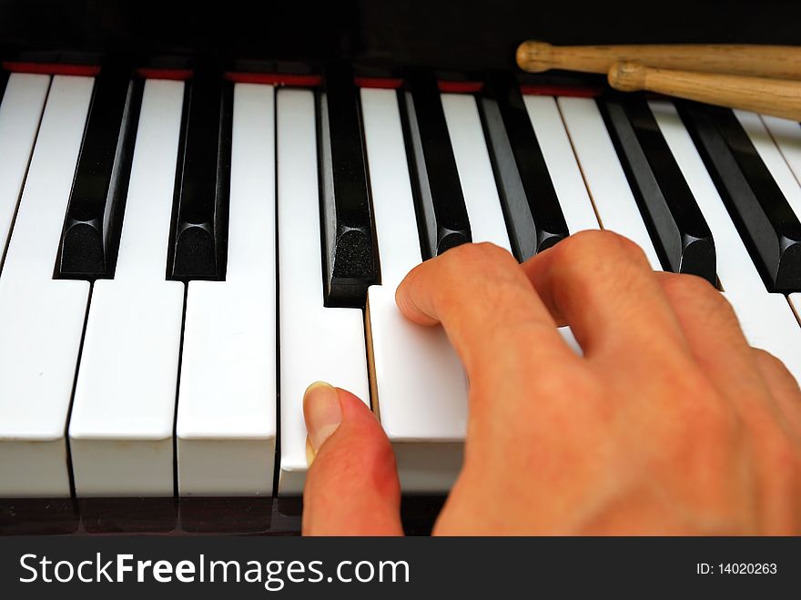 Right hand playing on black and white piano keyboard with drum sticks. For concepts like music and creativity. Right hand playing on black and white piano keyboard with drum sticks. For concepts like music and creativity.